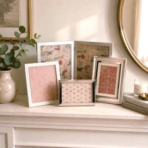 May include: A collection of four silver-toned metal picture frames of varying sizes and orientations. The frames display decorative inserts featuring patterns of pink stripes, floral motifs, and vintage-style botanical illustrations with butterflies.