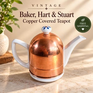 May include: A Baker, Hart & Stuart teapot featuring a polished copper body, a white ceramic handle, a white ceramic spout, and a white ceramic base. The lid is topped with a small white ceramic knob decorated with a blue floral pattern.