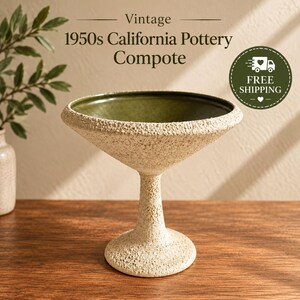 May include: A vintage 1950s California Pottery compote featuring a textured, off-white exterior finish and a smooth, deep olive green interior basin. The piece stands on a pedestal base with a wide, circular foot and a flared, open bowl top.