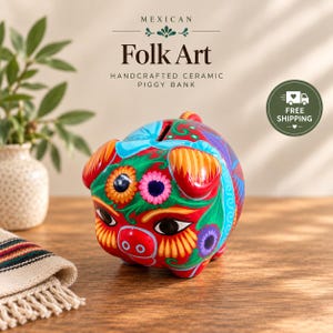 May include: A red ceramic piggy bank featuring intricate hand-painted floral patterns in blue, orange, and purple. The pig has large black eyes, a snout with two nostrils, and a coin slot on its back. The surface is glossy and brightly colored.