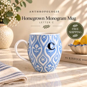 May include: A ceramic mug featuring a blue and white floral damask pattern with the letter C printed in black. The mug has a rounded body and a curved handle. Text on the mug reads Anthropologie Homegrown Monogram Mug Letter C.