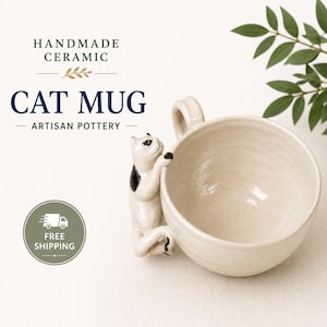 May include: A handmade ceramic mug in an off-white finish featuring a three-dimensional white cat with black spots climbing up the side. The text HANDMADE CERAMIC CAT MUG ARTISAN POTTERY is printed above the mug, with a circular icon below.