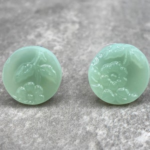 May include: A pair of round, green glass earrings with a floral design. The earrings are translucent and have a delicate, feminine look.
