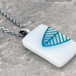 May include: A white glass pendant necklace with a teal leaf design. The necklace has a silver chain.