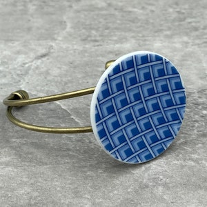 May include: A blue and white patterned ceramic circle attached to a gold metal bangle bracelet.
