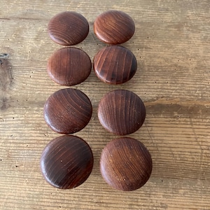 May include: Set of eight round wooden knobs with a dark brown finish. The knobs have a smooth, slightly textured surface.
