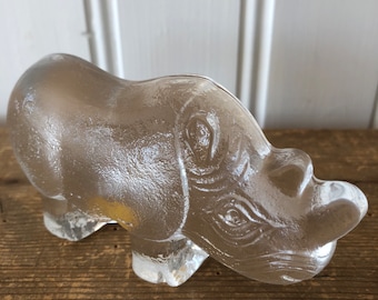 May include: A clear glass rhinoceros figurine. The rhinoceros is standing on all four legs and has a detailed face.