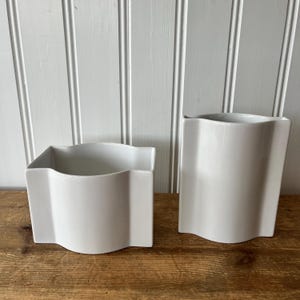 Peut inclure: Deux vases en céramique blanche avec une forme ondulée et organique. Les vases sont posés sur une surface en bois.