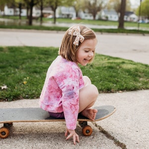 Toddler on a skateboard with a medium size sequins embellished bow in her hair.