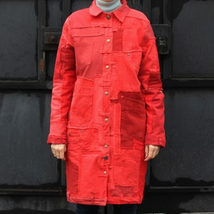 May include: A long red denim jacket with a button-up front and multiple pockets. The jacket is made of different pieces of denim sewn together.