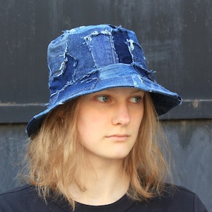 Pode incluir: Um chapéu de balde de brim azul feito de tecido patchwork. O chapéu tem uma aba larga e é usado por uma pessoa com cabelo comprido e loiro.