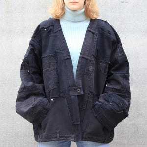 May include: A black denim jacket with a patchwork design. The jacket has a long, open front and a relaxed fit.