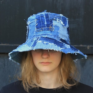 Pode incluir: Um chapéu de pescador de brim azul feito de tecido patchwork. O chapéu tem uma aba larga e é feito de diferentes tons de brim azul.