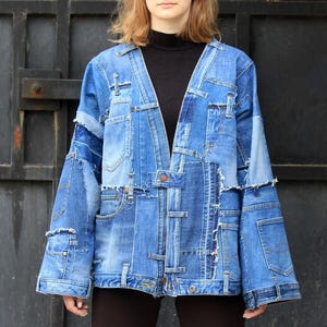 May include: A blue denim jacket with a patchwork design. The jacket has a V-neck and long sleeves. It is made of multiple pieces of denim sewn together.