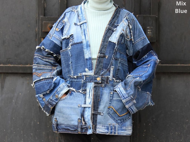 May include: A blue denim jacket made from patchwork denim with frayed edges. The jacket has a long, relaxed fit and a collarless design. The jacket is fastened with a button closure and has two pockets on the front.