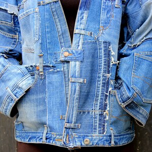 May include: A blue denim jacket made from multiple pieces of denim sewn together. The jacket has a frayed and distressed look, with visible stitching and seams.