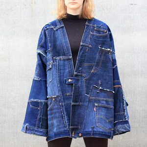May include: A dark blue denim jacket made from patchwork pieces of denim. The jacket has a long, loose fit and a collarless design.