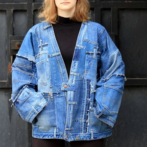 May include: A patchwork denim jacket constructed from various shades of blue jeans, featuring a V-neckline, long sleeves, and visible frayed seams. The garment is composed of multiple denim panels with integrated pockets and metal button details.