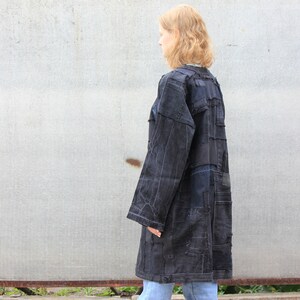 Pode incluir: Uma jaqueta de ganga azul escura comprida com um design de patchwork. A jaqueta &eacute; feita de diferentes peda&ccedil;os de ganga costurados juntos, criando um visual &uacute;nico e texturizado.