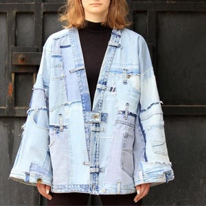 May include: A light blue denim jacket made from patchwork pieces of denim. The jacket has a long, loose fit and a relaxed silhouette. It features a button-up front closure and a collar.