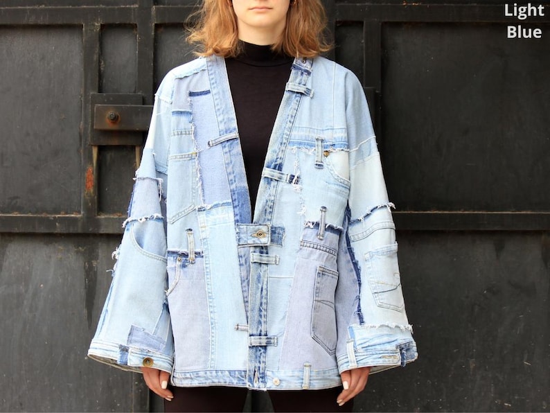May include: A light blue denim jacket made from patchwork pieces of denim. The jacket has a long, loose fit and a relaxed silhouette. It features a button-up front closure and a collar.