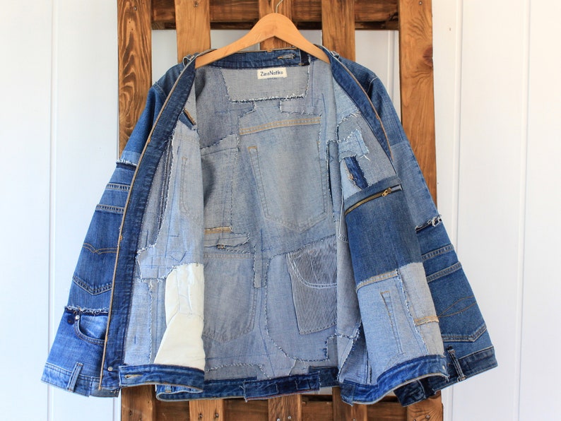May include: A blue denim jacket with a patchwork design. The jacket is unzipped and the inside is lined with different shades of blue denim. The jacket has a zippered pocket on the right side.