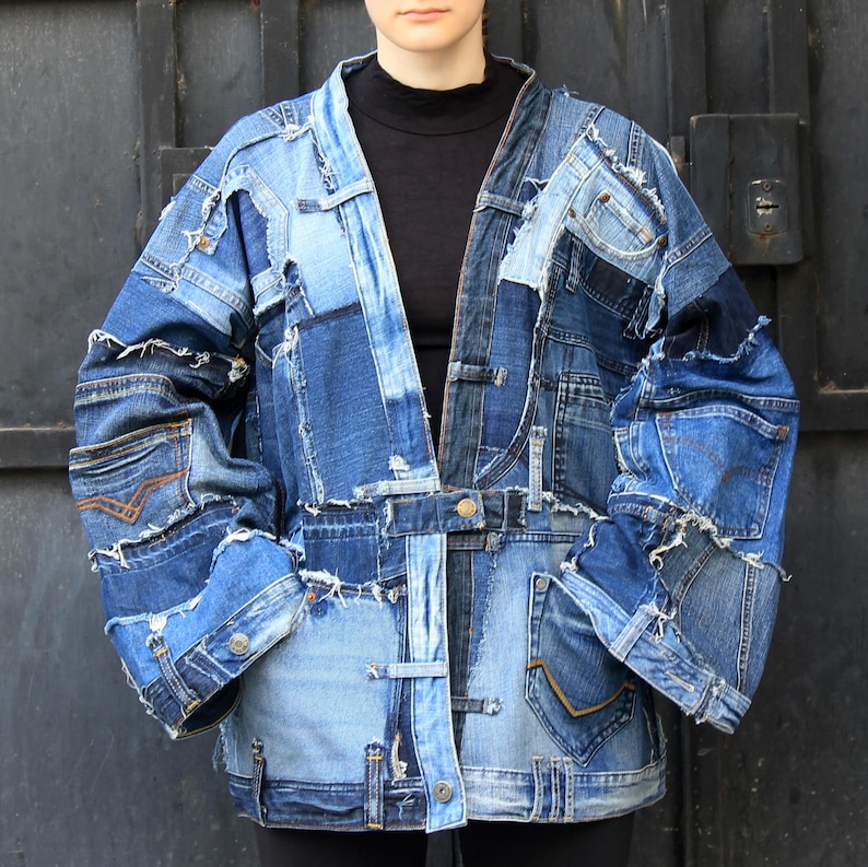 May include: A blue denim jacket made from patchwork pieces of different denim fabrics. The jacket has a long, loose fit and a collarless design. The jacket is made with a variety of denim washes and textures, including light blue, dark blue, and indigo.