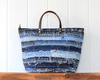 Może przedstawiać: Duża torba typu tote wykonana z recyklingowanego denimu. Torba jest niebieska i ma brązowy skórzany uchwyt. Torba jest wykonana z wielu różnych kawałków denimu zszytych ze sobą.