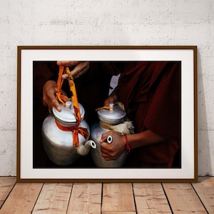 May include: Two silver teapots with lids and handles, held by two people wearing red robes. The teapots have orange and yellow fabric tied around them.