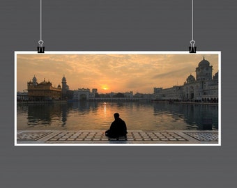 May include: A silhouette of a person sitting on a tiled platform in front of a golden temple reflecting in a still body of water at sunrise.