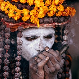 This fine art print captures a Naga Sadhu at the Kumbh Mela in Near Varanasi, India. The image showcases their unique attire and spiritual practice of smoking a chilum