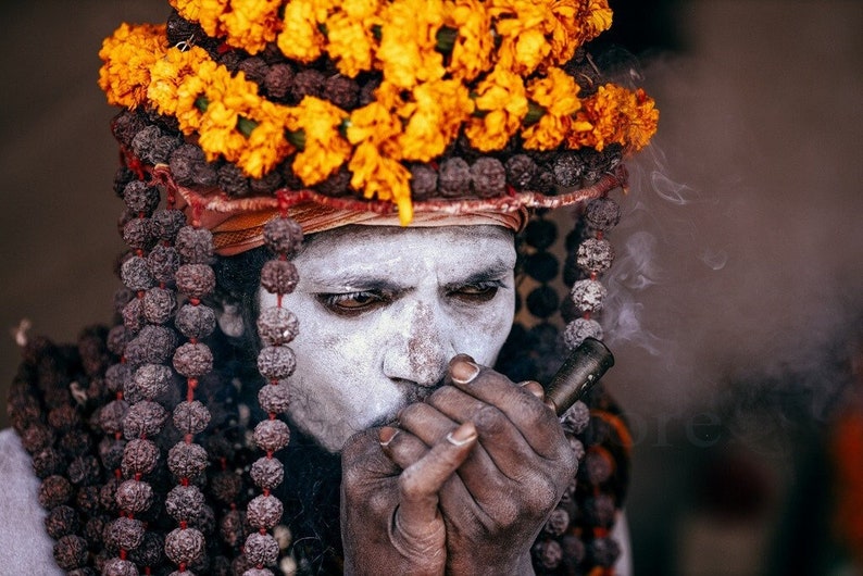 This fine art print captures a Naga Sadhu at the Kumbh Mela in Near Varanasi, India. The image showcases their unique attire and spiritual practice of smoking a chilum