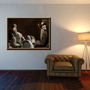 May include: A group of people wearing white robes gather in a dimly lit room. One person holds a lit candle and stands in the center of the group. The room has a stone wall and a wooden door.