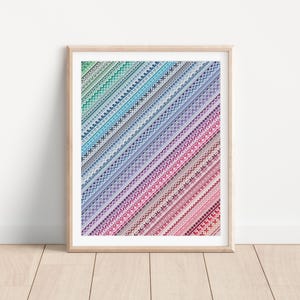 May include: A framed print with a colorful geometric pattern. The pattern is made up of diagonal lines of different colors and textures. The colors in the pattern are blue, green, purple, pink, and red.