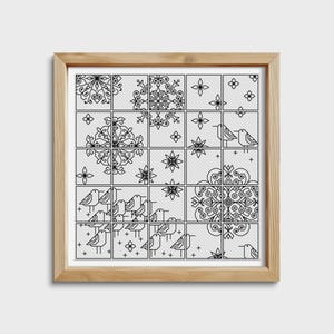 May include: A framed cross-stitch artwork featuring a grid of squares with black and white designs. The designs include floral patterns, snowflakes, and stylized birds. The frame is made of light-colored wood.
