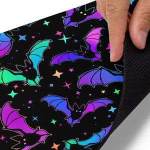 May include: A black mouse pad with a repeating pattern of rainbow bats and stars. The mouse pad is made of a soft, non-slip material.