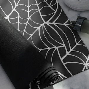 May include: Black yoga mat with a white spiderweb design. The mat is rolled up and the design is visible on the outside of the roll.