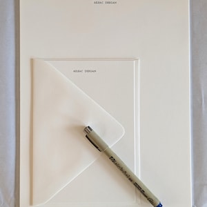 May include: A set of off-white stationery including a large sheet of paper and a smaller envelope, both featuring the printed name AILEAC DEEGAN in black ink. A grey Pigma Micron 05 pen with a blue cap is placed diagonally across the envelope.