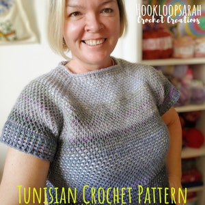 Può includere: Una donna indossa un top in crochet tunisino con gradiente di colore grigio e blu, con maniche corte. Il testo "HOOKLOOPSARAH Crochet Creations" e "TUNISIAN CROCHET PATTERN" sono visibili nell'immagine.
