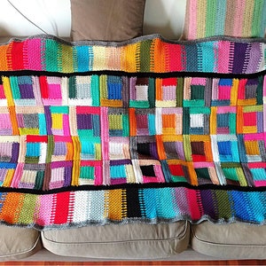 Puede incluir: Una manta de crochet colorida con un diseño de patchwork que presenta cuadrados de varios colores, incluidos rojo, azul, verde, amarillo y morado. La manta tiene un borde negro y una franja gris.