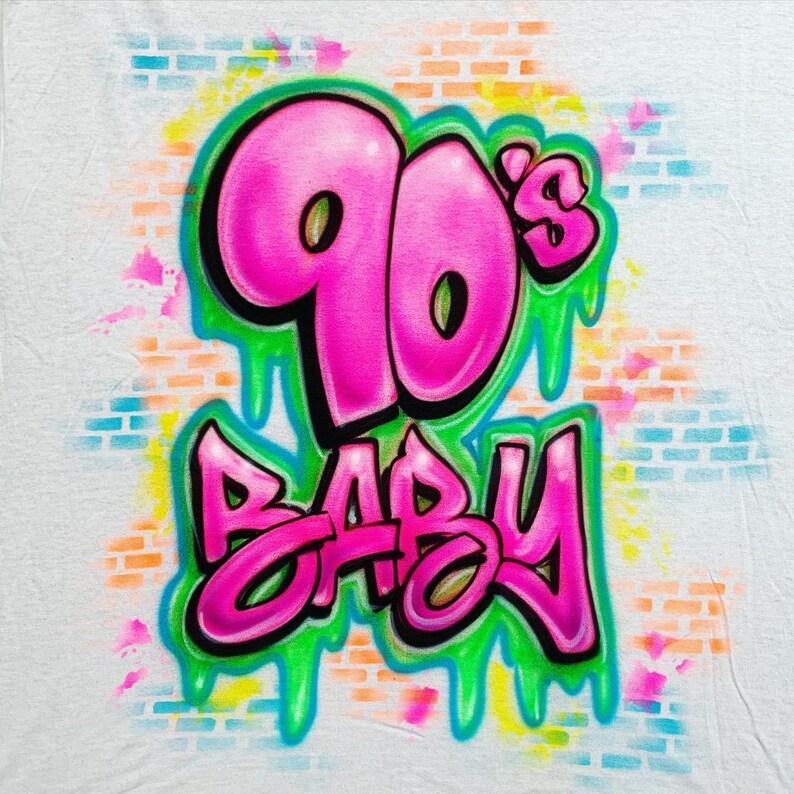 May include: A white t-shirt with a pink and green graffiti design that says "90's Baby".