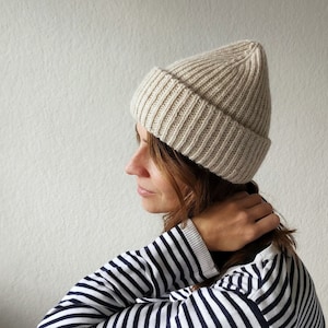 Könnte beinhalten: Eine Frau trägt eine beige Strickmütze und einen gestreiften schwarz-weißen Pullover.