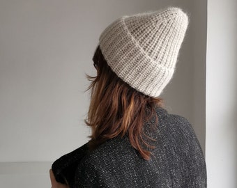 May include: A light beige knitted beanie with a slouchy fit. The beanie is made of a soft, fuzzy yarn.