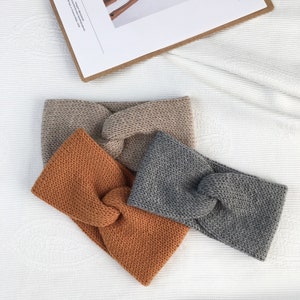 Könnte beinhalten: Drei gehäkelte Stirnbänder in verschiedenen Farben: Beige, Orange und Grau. Die Stirnbänder sind verknotet und haben ein schlichtes, minimalistisches Design.
