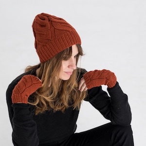以下が含まれることがあります： さび色のニット帽とフィンガーレスグローブのセット。帽子はケーブルニットの模様で、手袋はシンプルなニットの模様です。
