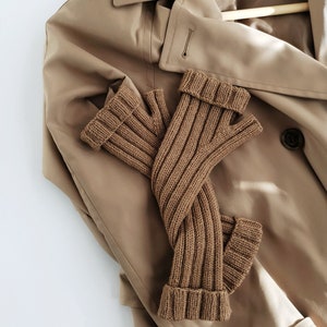 Könnte beinhalten: Ein Paar braune gestrickte Fingerhandschuhe auf einem beigefarbenen Trenchcoat.