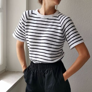 以下が含まれることがあります： 白と黒のストライプの半袖シャツと黒いショートパンツを合わせたコーディネート。ショートパンツはゴムウエストでポケット付きです。