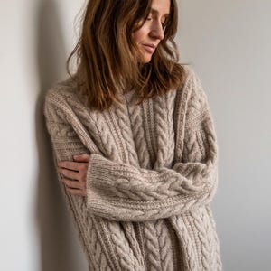 Peut inclure: Un pull en maille torsadée beige à la coupe ample. Le pull est fait d'un tissu doux et confortable et a un style décontracté et détendu.