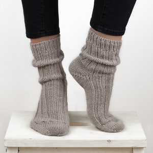 Pode incluir: Um par de meias de l&atilde; cinzas com textura canelada. As meias s&atilde;o de tornozelo e s&atilde;o usadas nos p&eacute;s de uma pessoa.