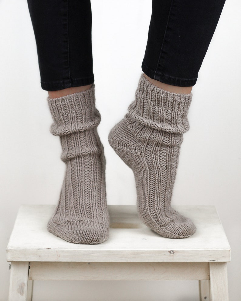 Pode incluir: Um par de meias de l&atilde; cinzas com textura canelada. As meias s&atilde;o de tornozelo e s&atilde;o usadas nos p&eacute;s de uma pessoa.